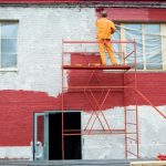 homme peignant une façade en rouge