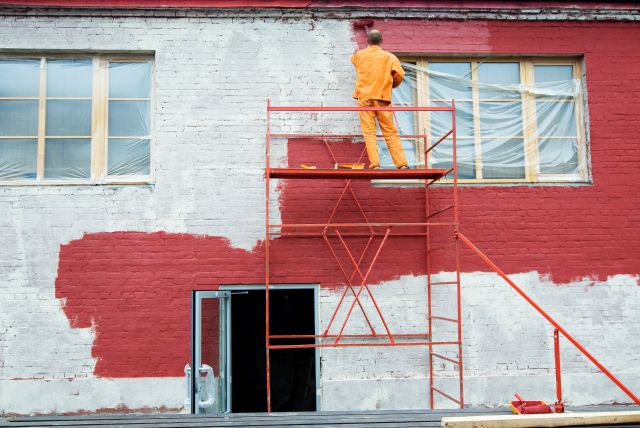 homme peignant une façade en rouge